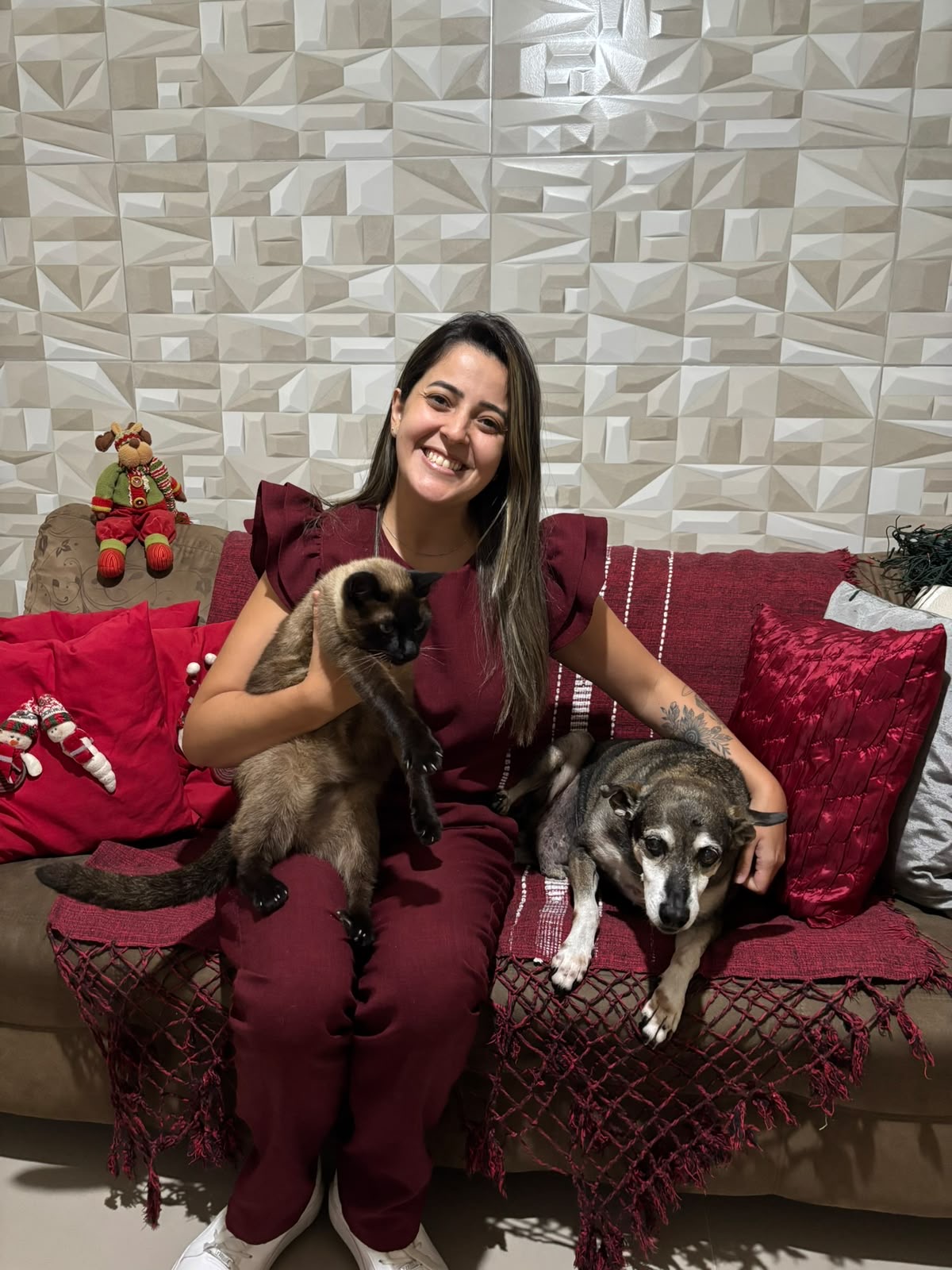 M.V. Nathana Carregoza no sofá com um gato e um cachorro idoso atendidos em casa