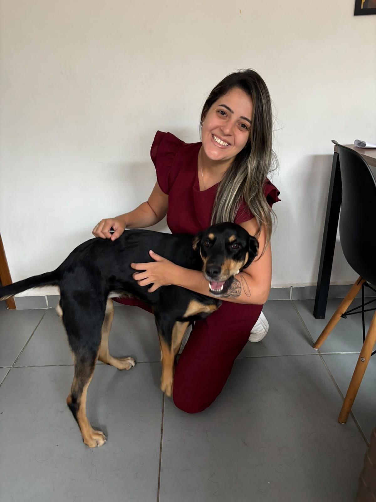 M.V. Nathana Carregoza agachada ao lado de um cachorro preto durante o atendimento